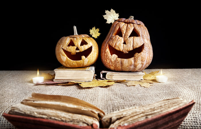 Two evil looking pumpkins sitting on top a pile of books