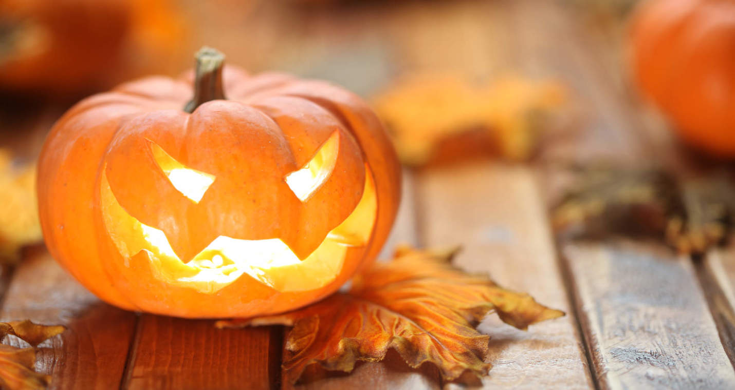 A small pumpkin sitting in the dark with an evil grin