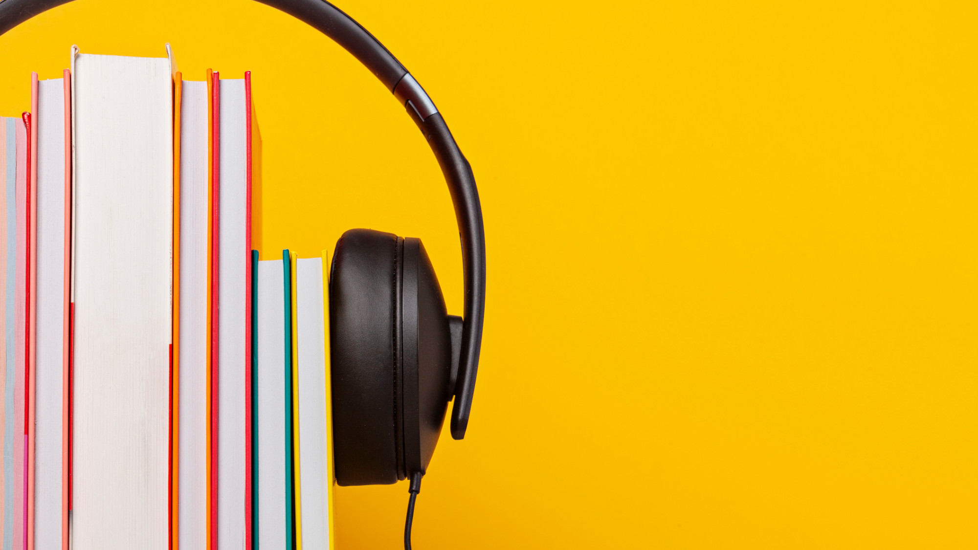 An image of books in a row in between headphones with a yellow background.