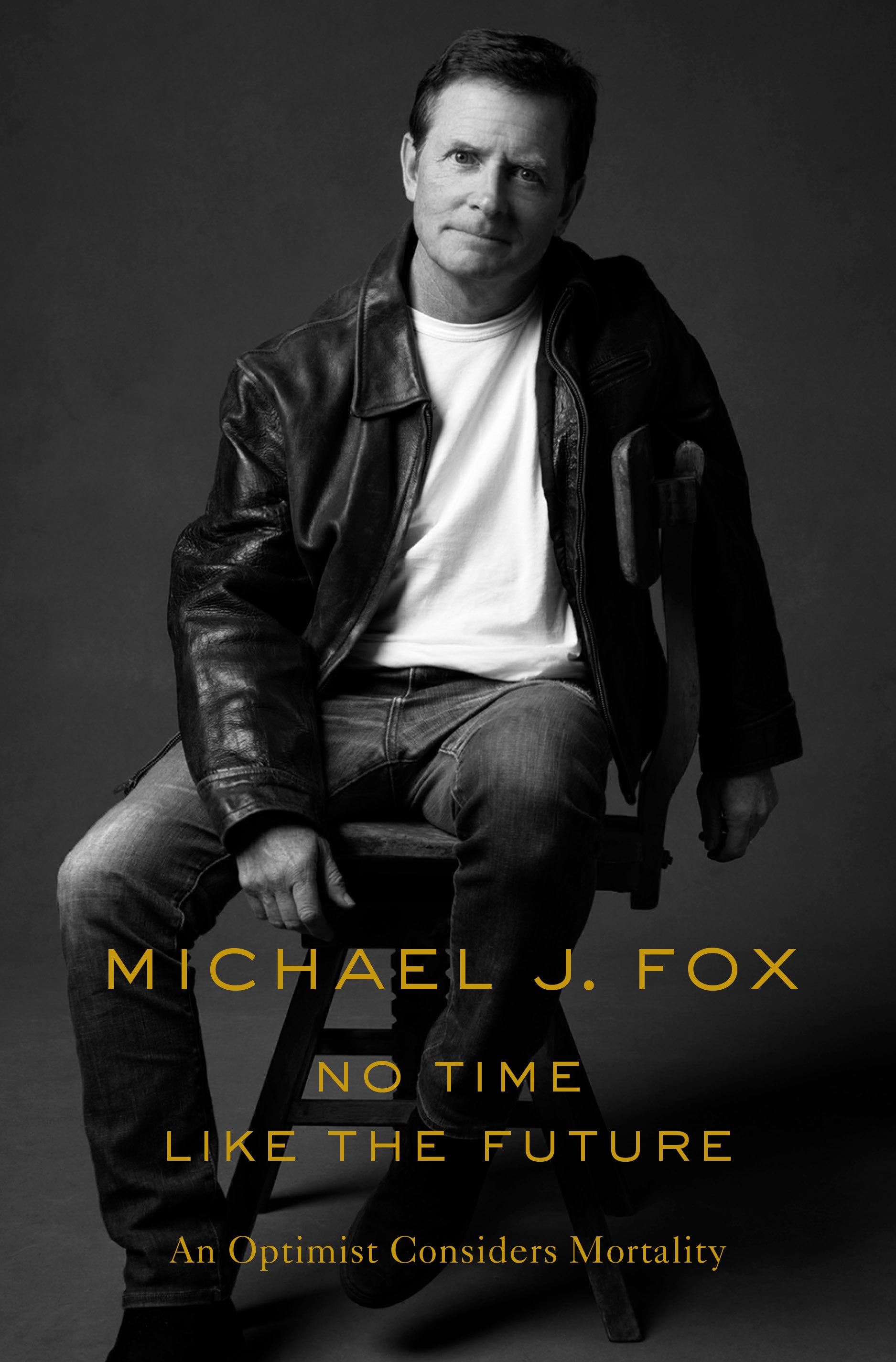 A black and white bookcover with Michael J. Fox sitting on a stool with orange text that reads "No Time Like the Future: An Optimist Considers Mortality."