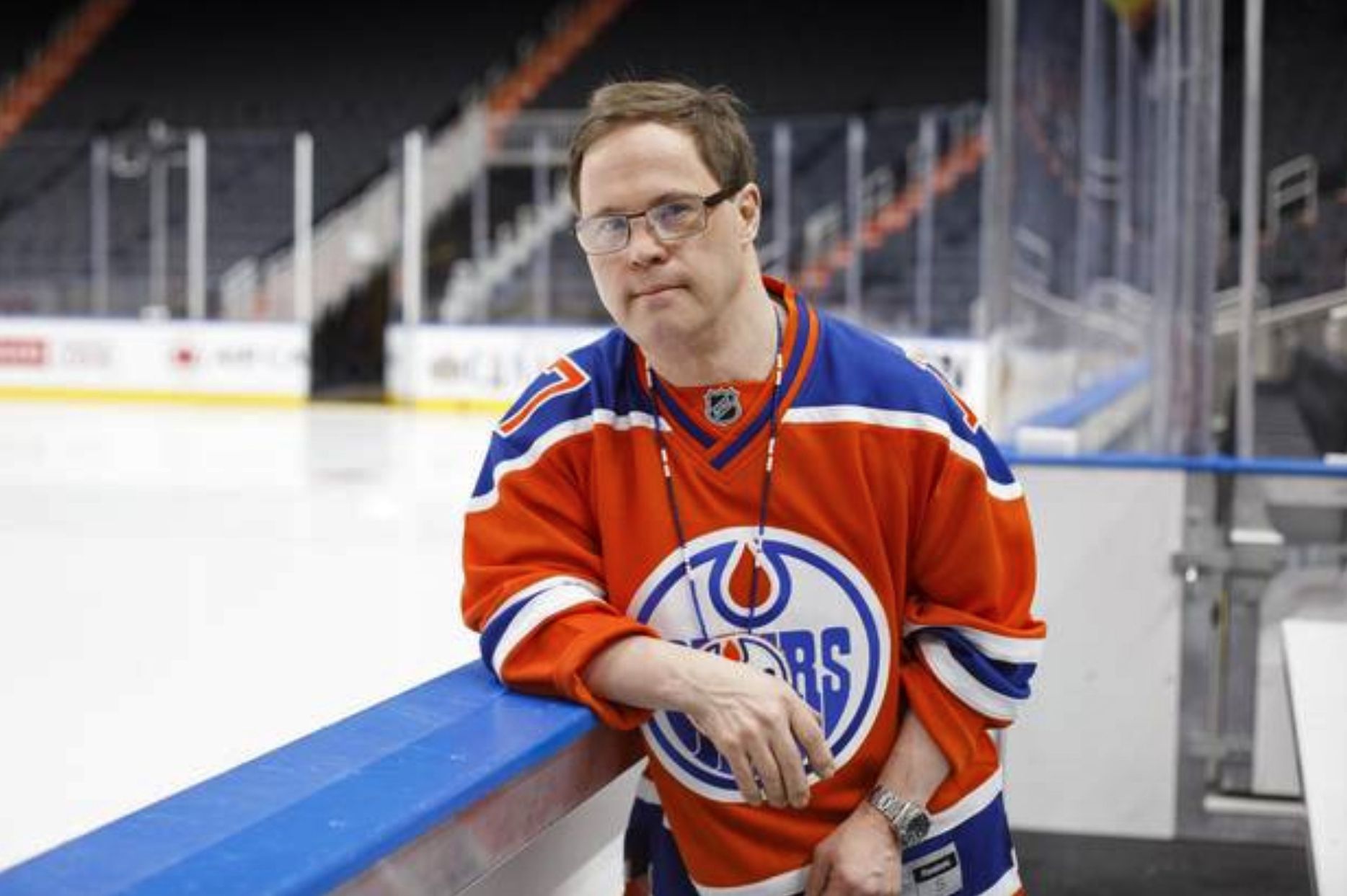 A photo of Joey Moss wearing an Edmonton Oilers jersey posing beside an ice hockey rink. 