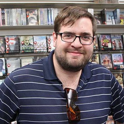 A photo of Michael McNeely smiling in a video store. 