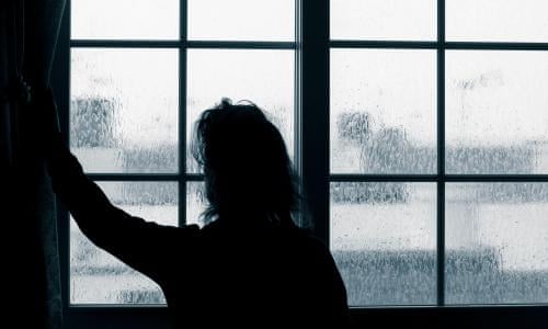A silhouette of a person indoors looking outisde a window.
