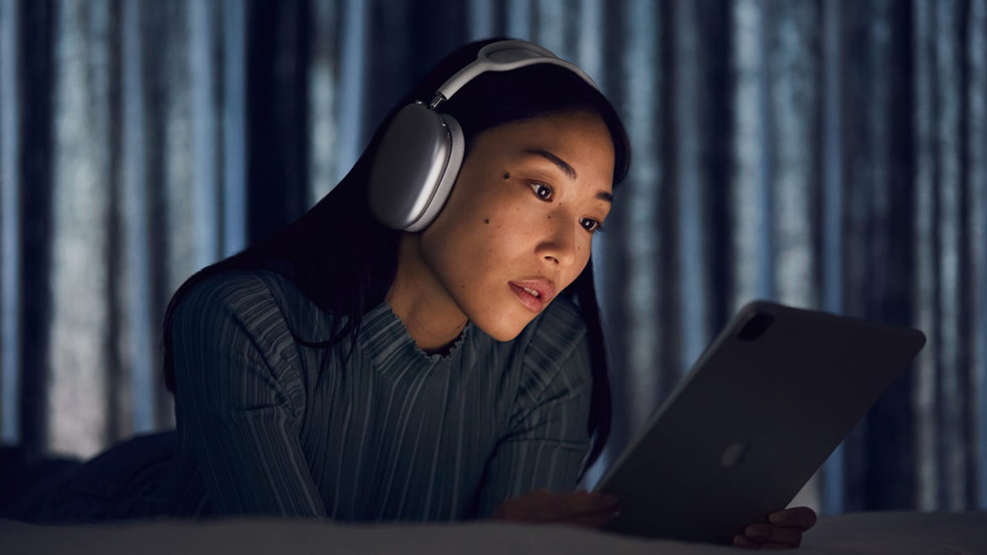 A woman wearing AirPodsMax in the dark while watching her tablet.