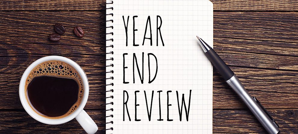 An overhead shot of a cup of coffee, pen, and a notebook with handwriting that reads "Year End Review." 