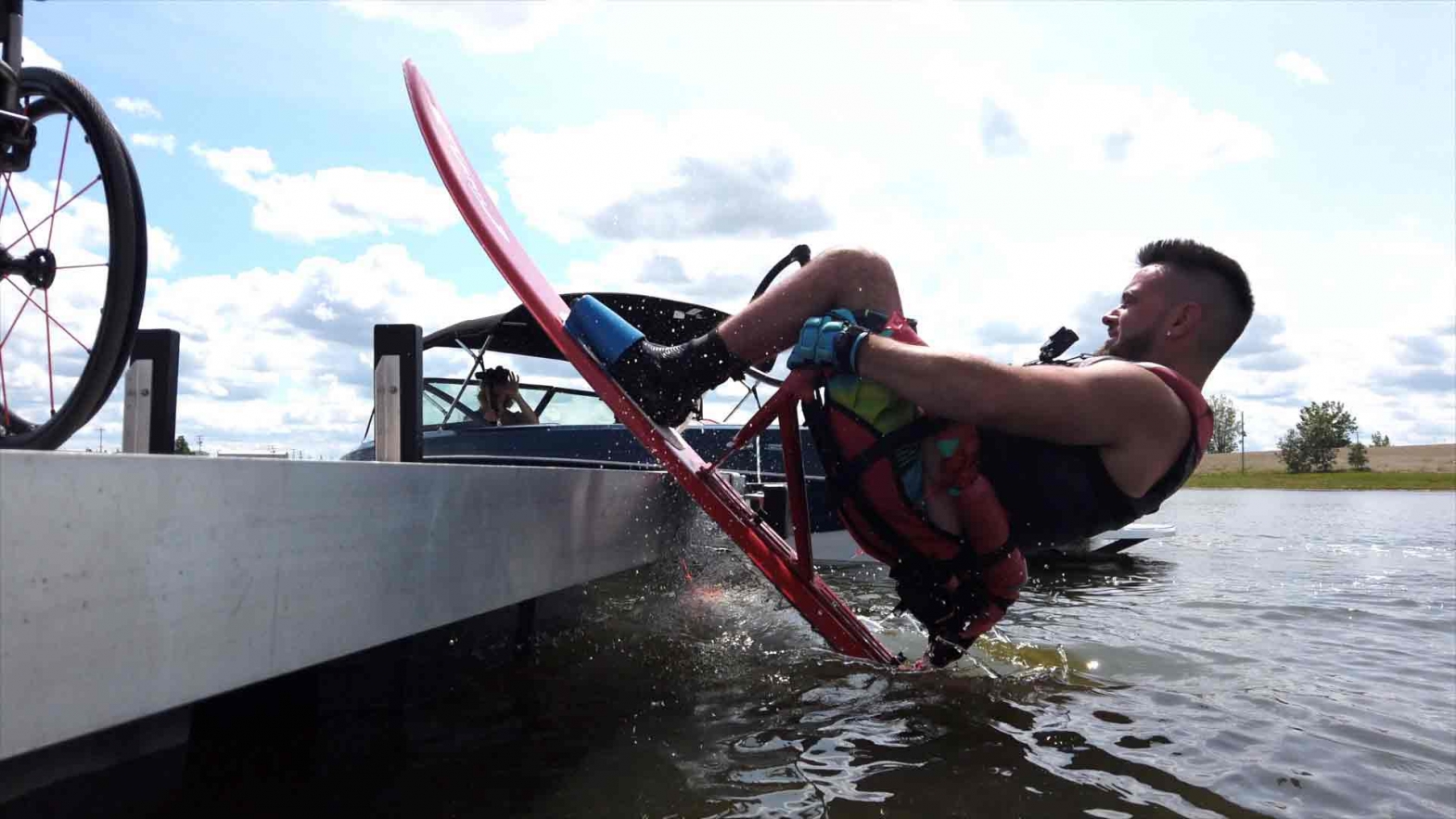 A man with a disability rolls backward into a lake from a dock while strapped and seated in his water sled. 