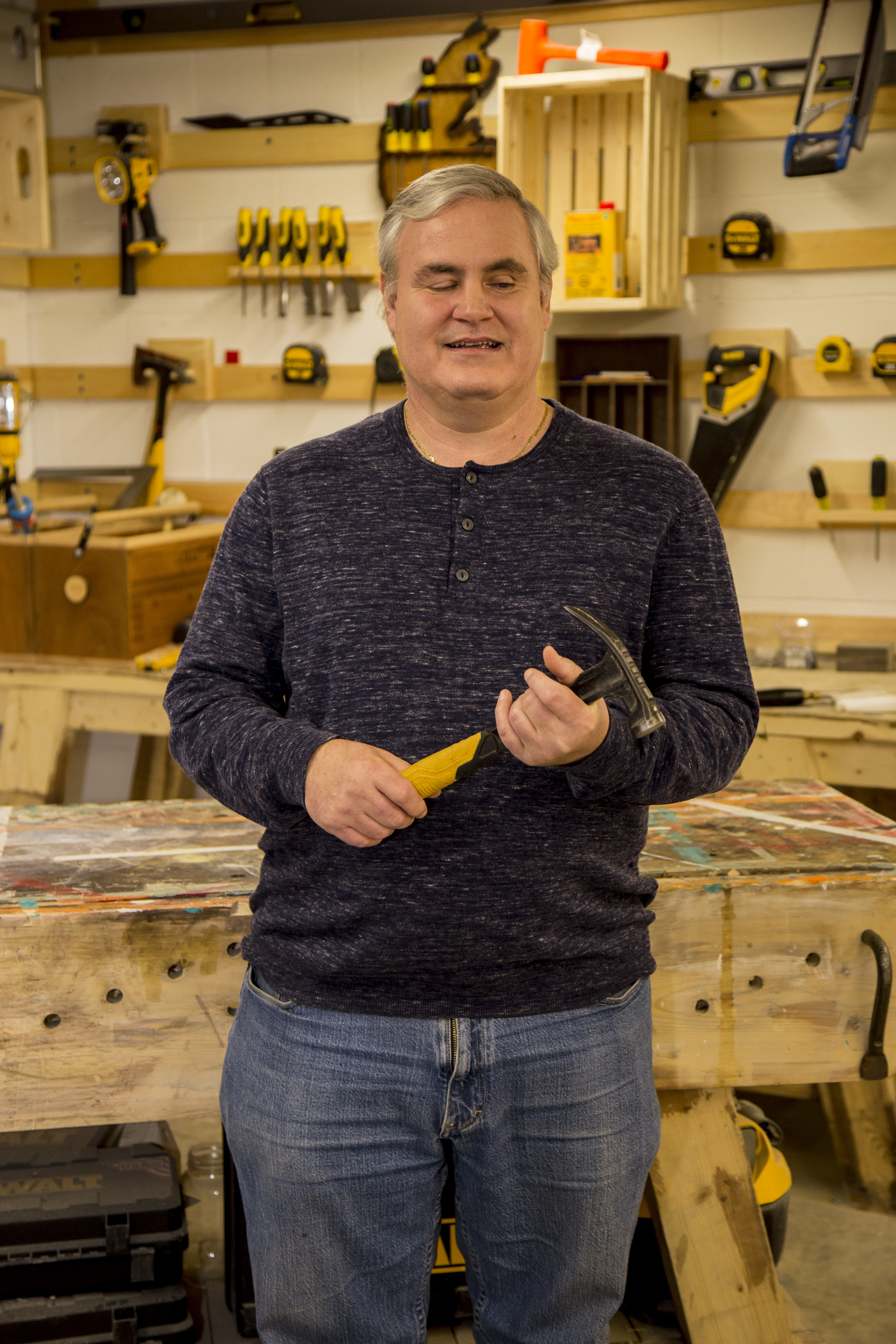 Blind Handyman Chris Judge smiling in a workshop while holiding a hammer in hands. 