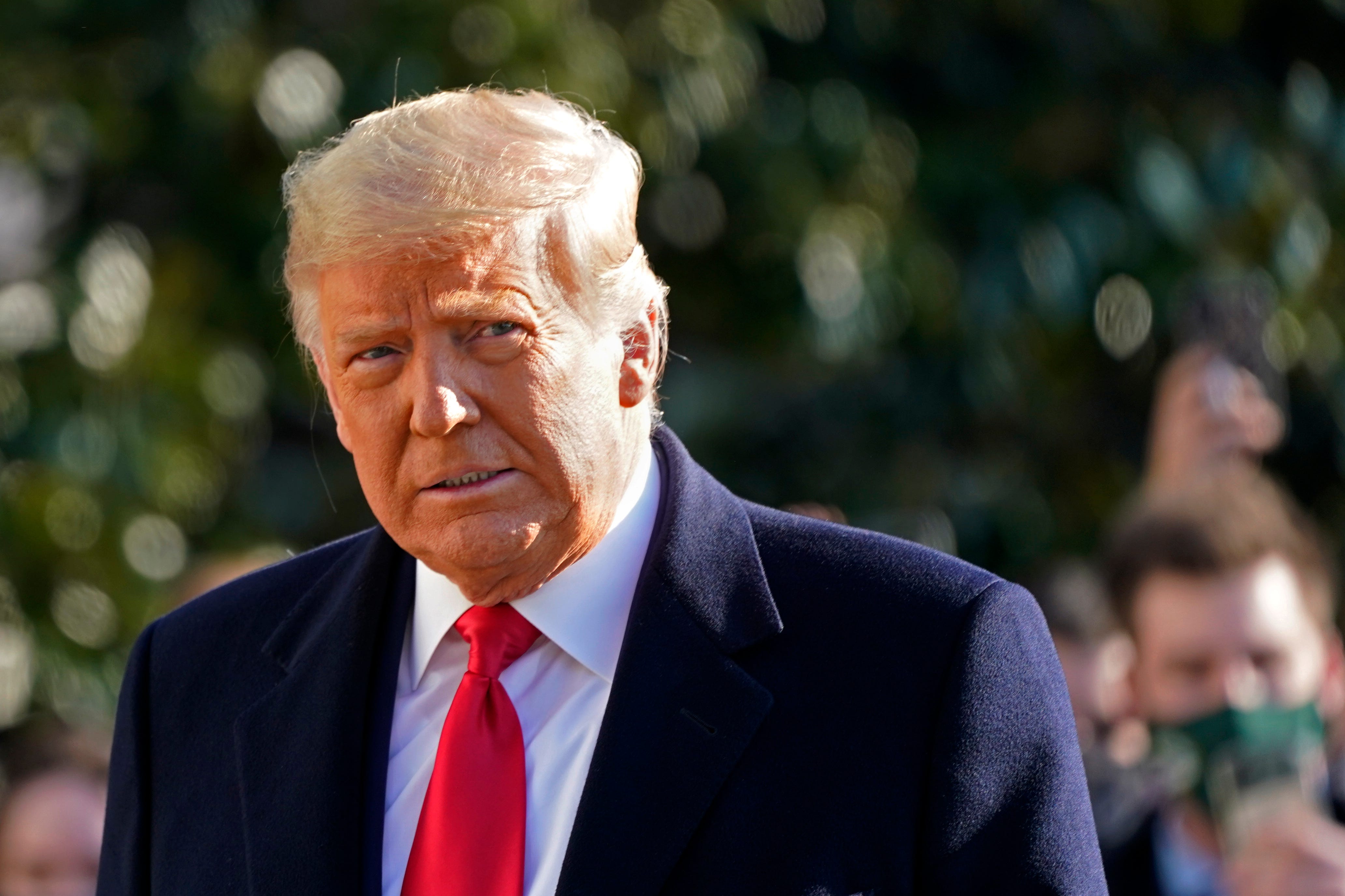 A photo of Donald Trump outisde  in a suit with a red tie. 