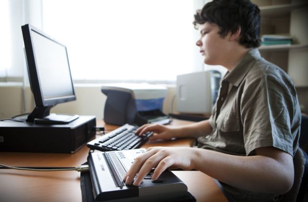 A person who is blind using a computer desktop with a braille reader.