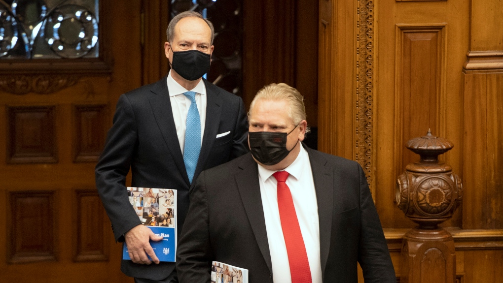 A photo of Finance Minister Peter Bethlenfalvy and Doug Ford walking side by side with masks and books in their hands. 