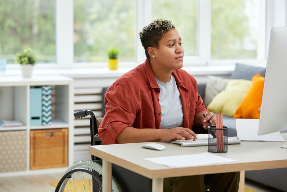 A woman in a wheelchair typing at her work desk.