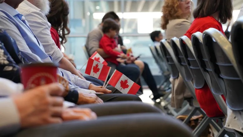 A closeup of people's laps sitting in a row. Some people are holding mini Canadian flags.