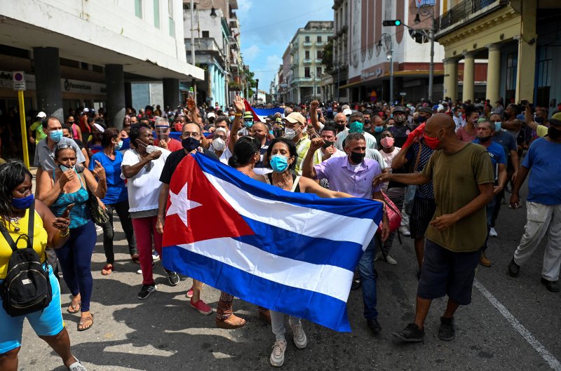  Thousands of Cubans wearing face masks march in protest against the communist government. A woman leads the crowd with a Cuban in her hands. 