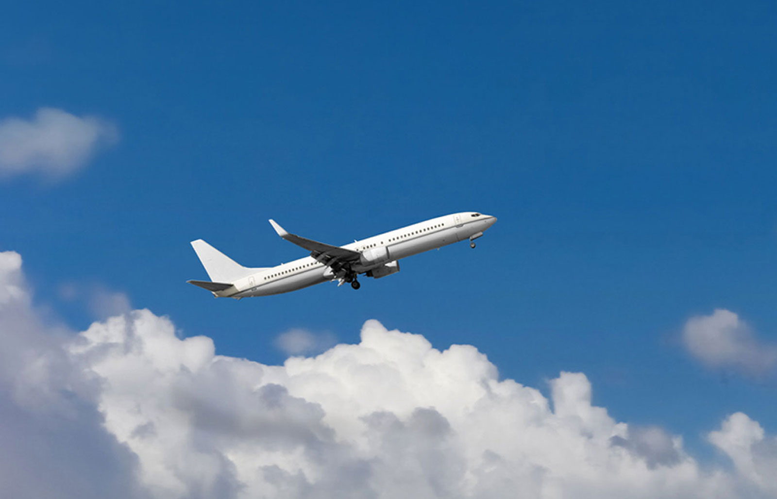 A white plane flying in a blue sky with white clouds. 
