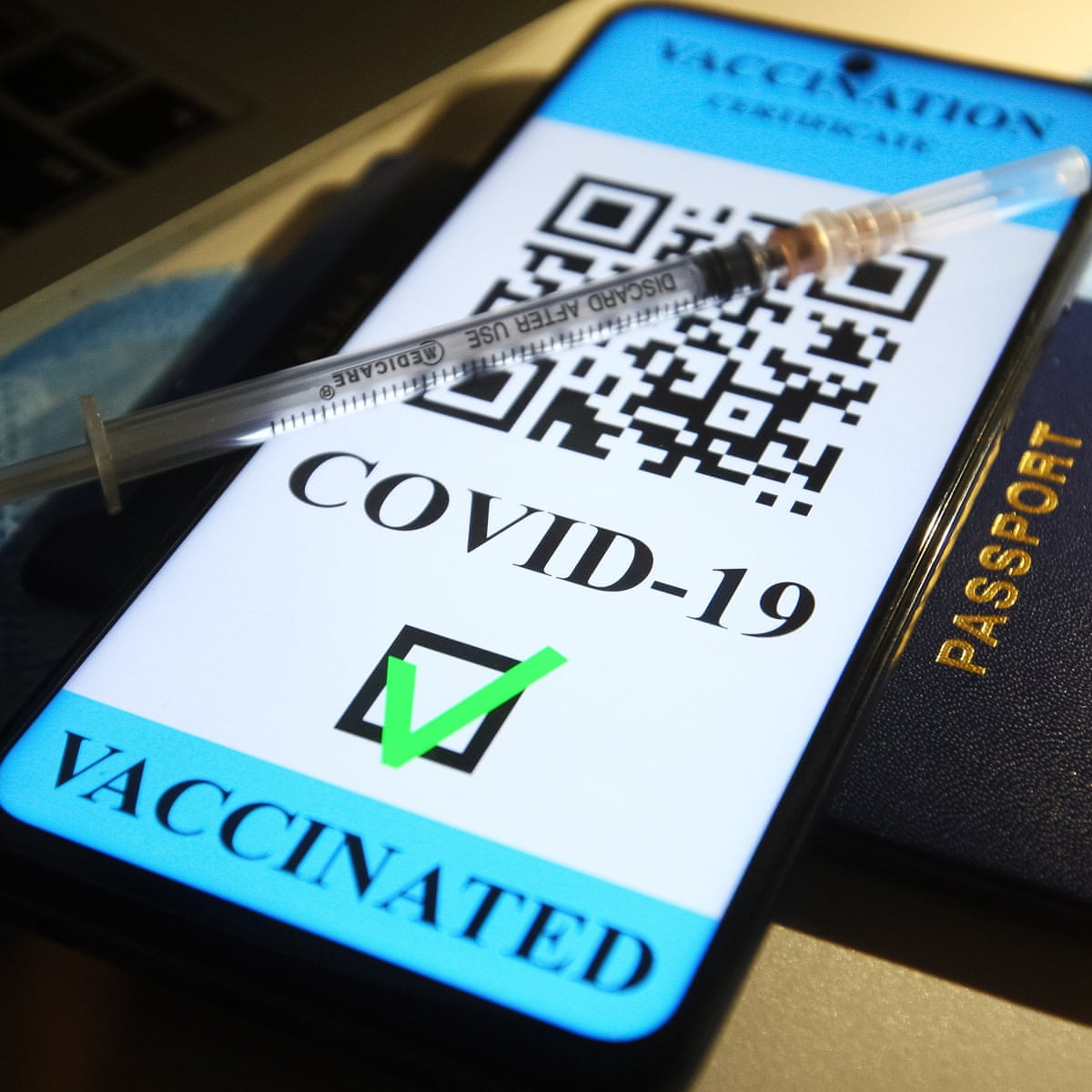 Image shows a phone placed on a passport with the vaccine passport app open. And a needle placed on the phone.