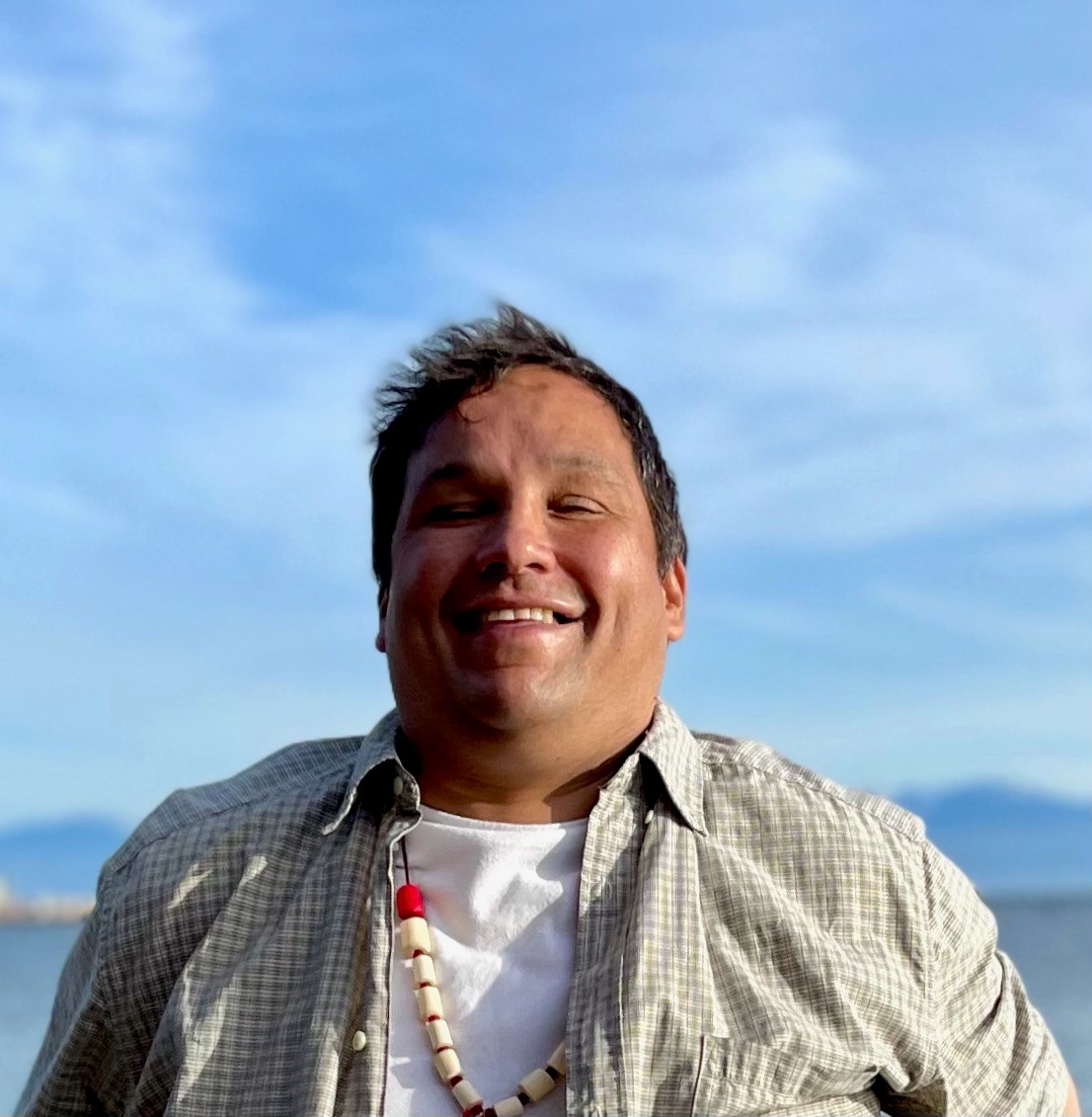 A photo of Shane Baker smiling with a bright blue sky behind him.