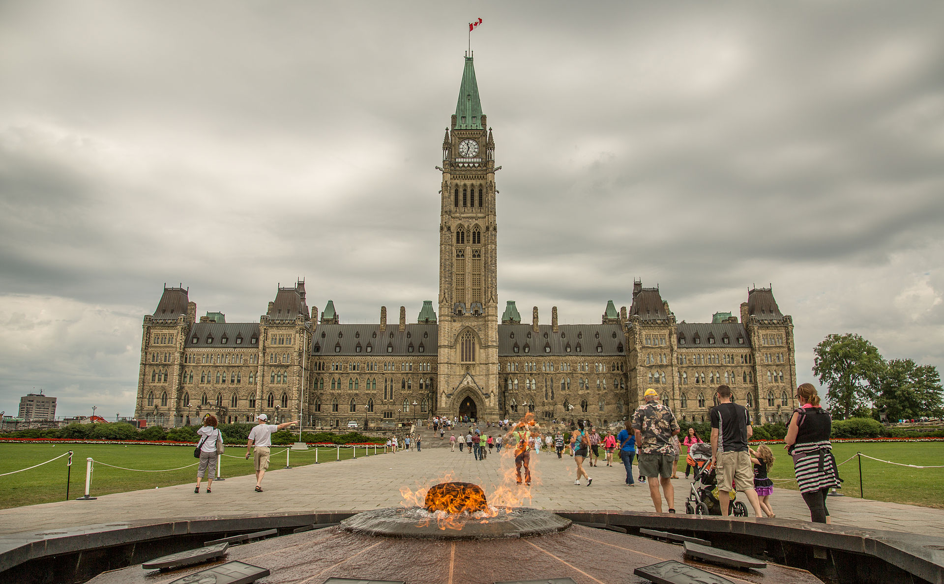 A photo of a fire monument in Ottawa with the the parliament building in occupying most of the photo in the background.