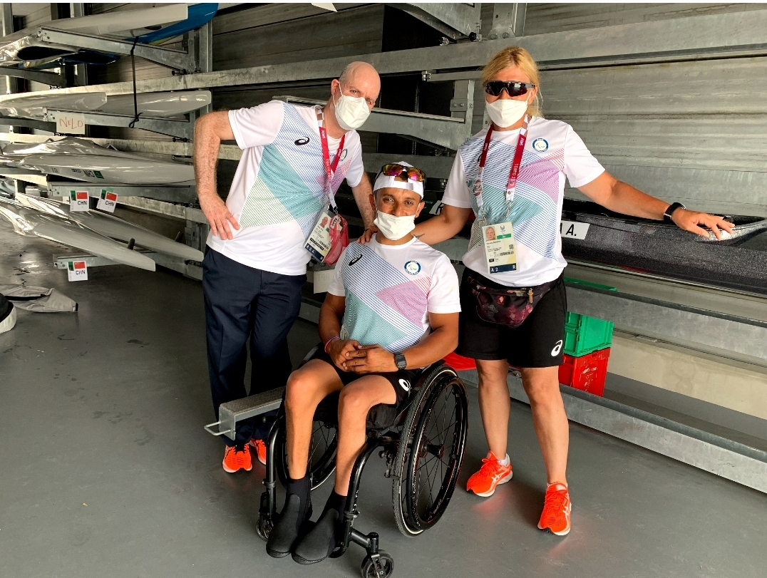 A photo of Refugee Paralympic Team athlete Anas Al Khalifa sitting in his wheelchair between his standing coach and Teddy Katz. All three are wearing face masks. 