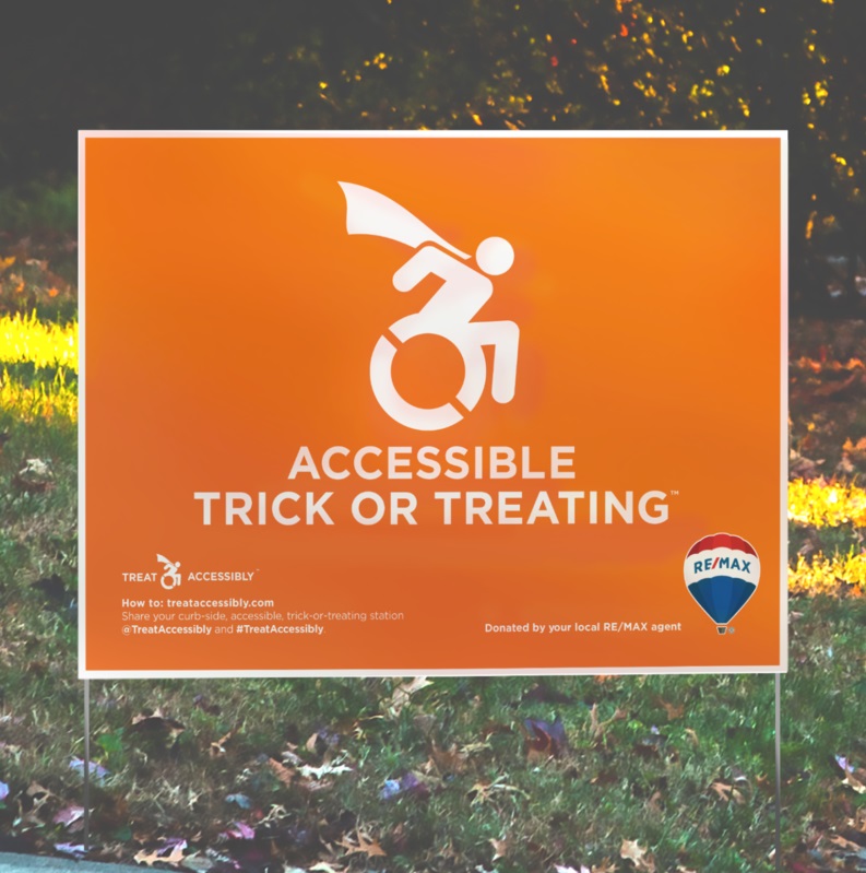 An orange lawn sign with a white universal symbol of access in motion with a cape. The text reads "accessible trick or treating." The bottom right is a Remax logo of a red, white and blue blimp. 