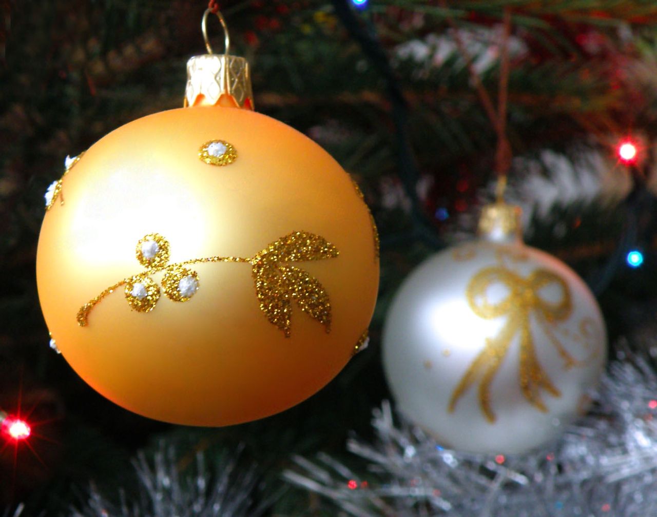 A golden ornament and a silver ornament hanging in a Christmas tree.