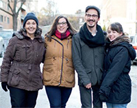 ​​Denise, Sonia, Étienne et Maude bras dessus, bras dessous sont debout dans une rue et sourient en fixant l'objectif.