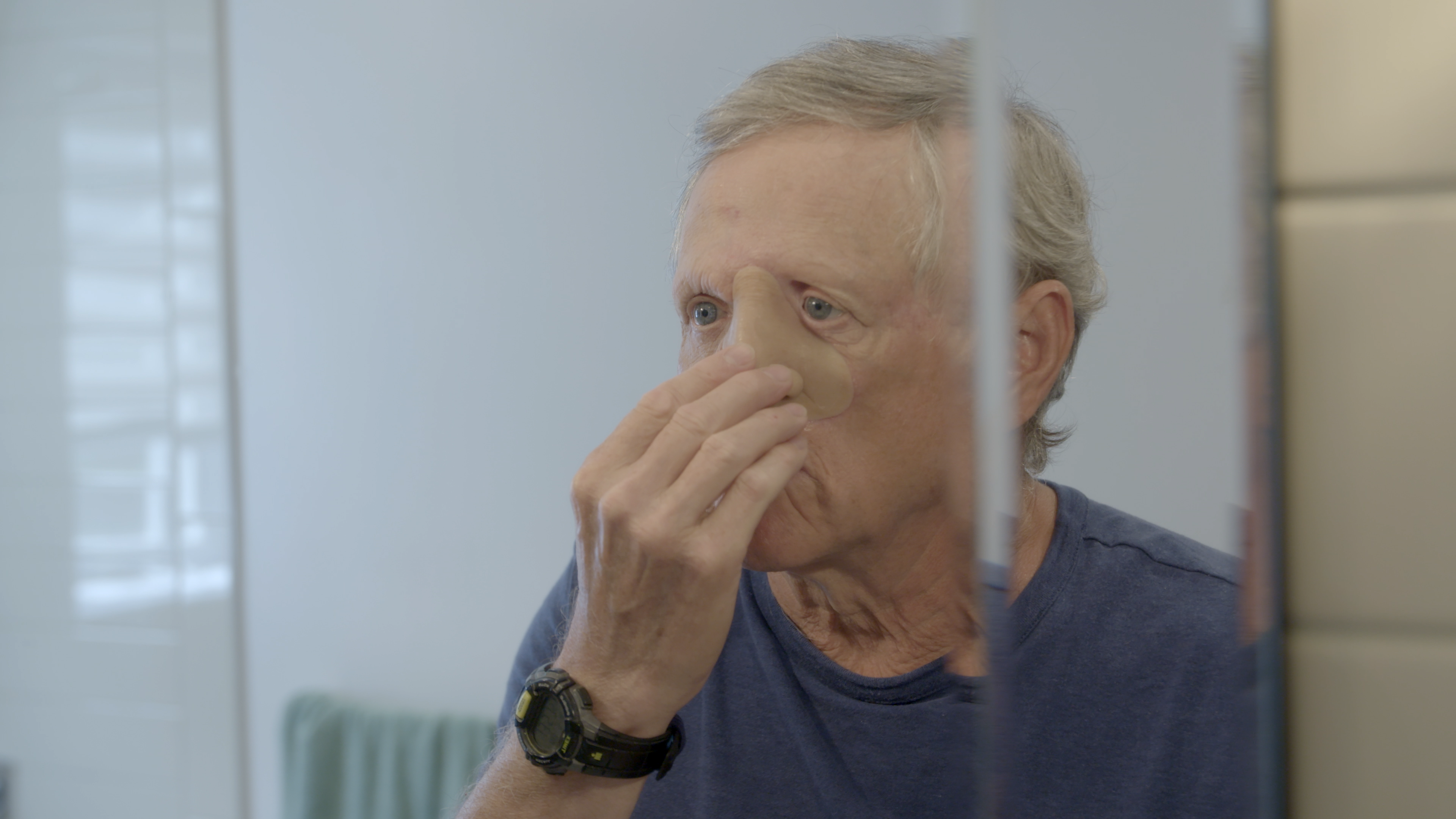Un homme tient une prothèse de nez sur son visage en se regardant dans le miroir.
